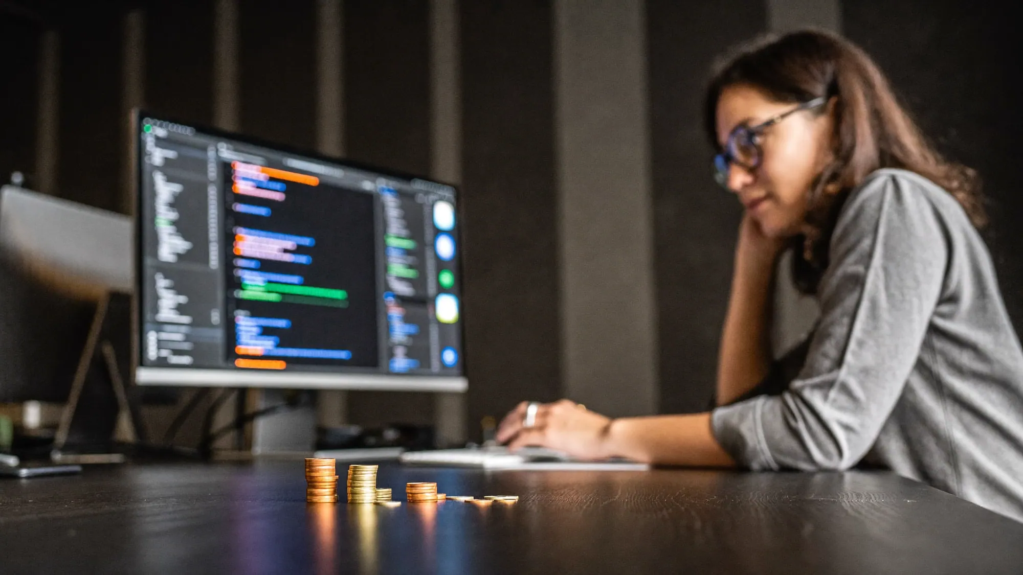 A developer with code on screen and coins, representing custom software development cost