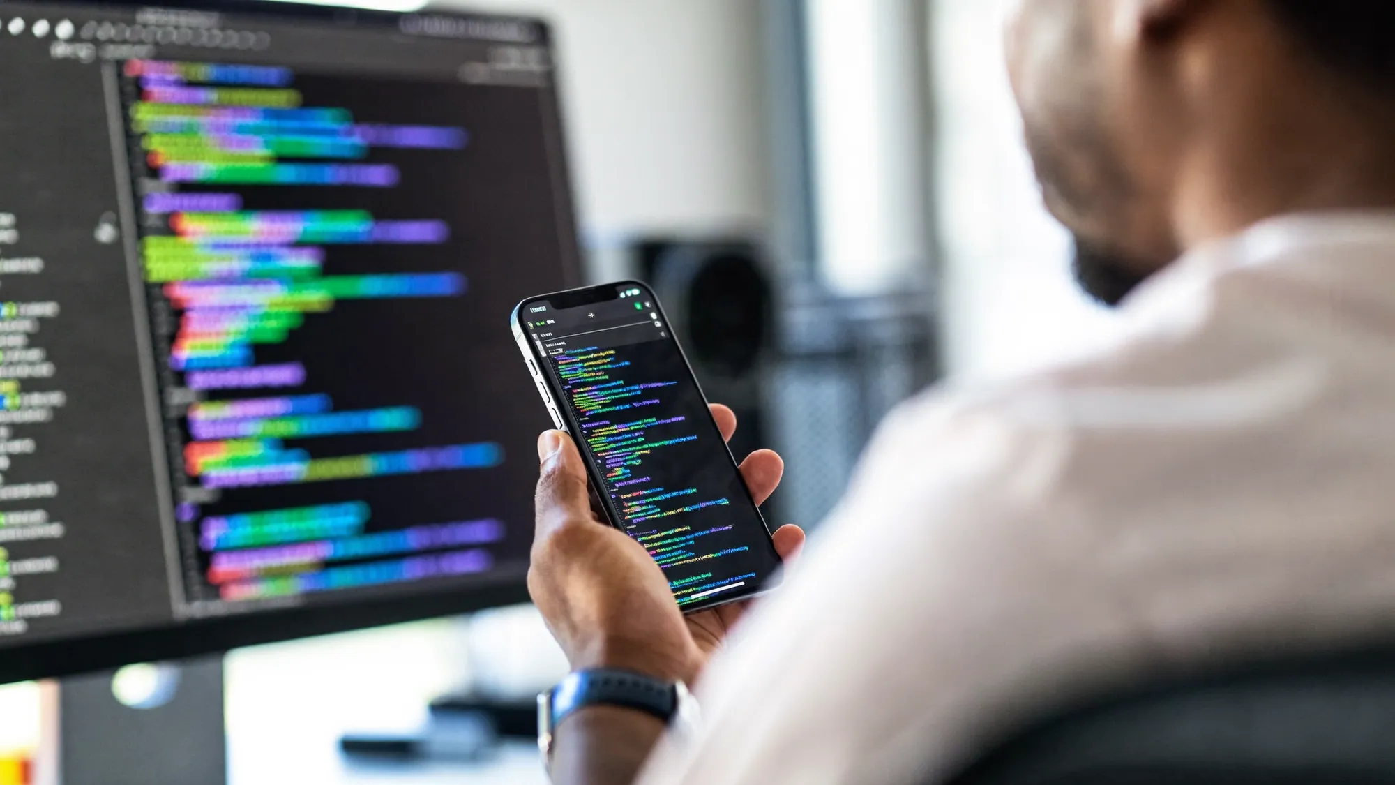 A developer building a mobile app with a phone and code on screen, illustrating how to build a mobile app