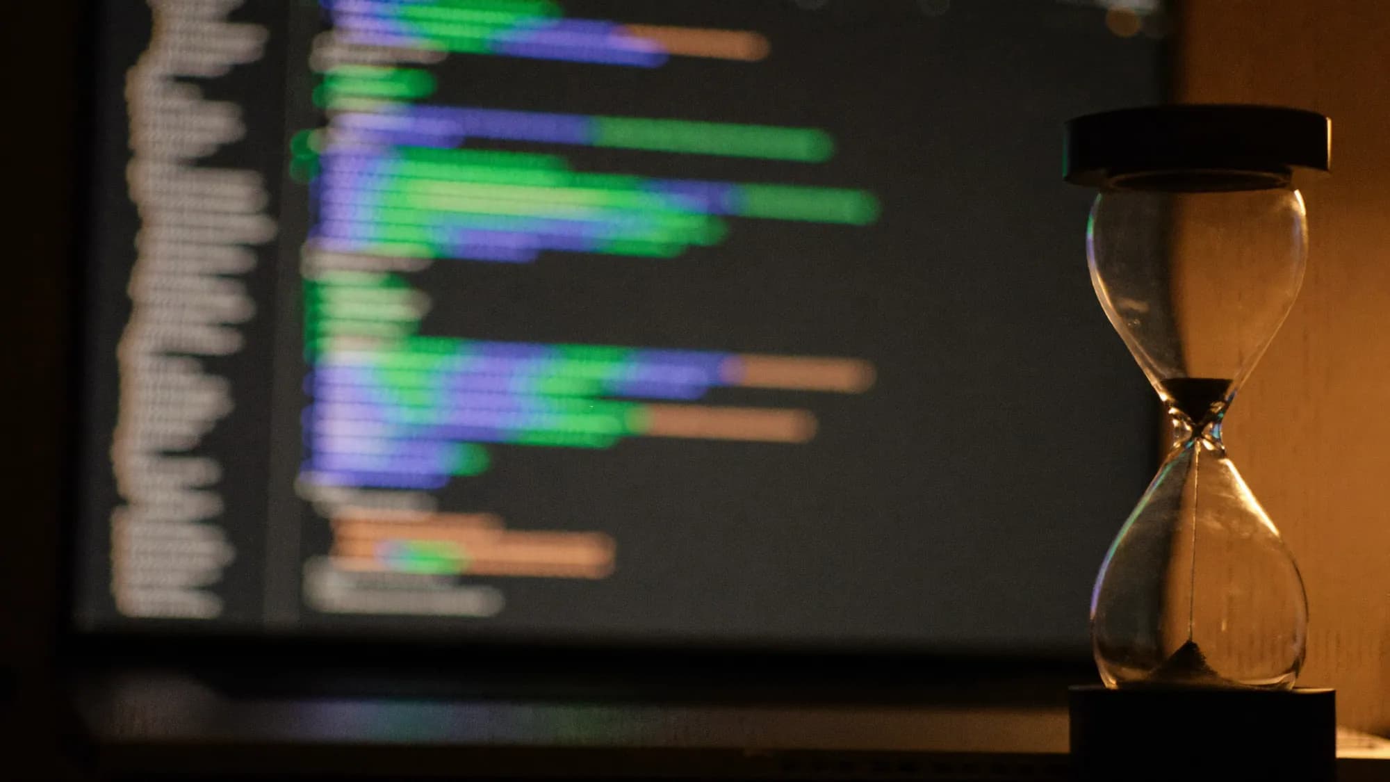 Code on a monitor beside an hourglass, a metaphor for how long it takes to build a website