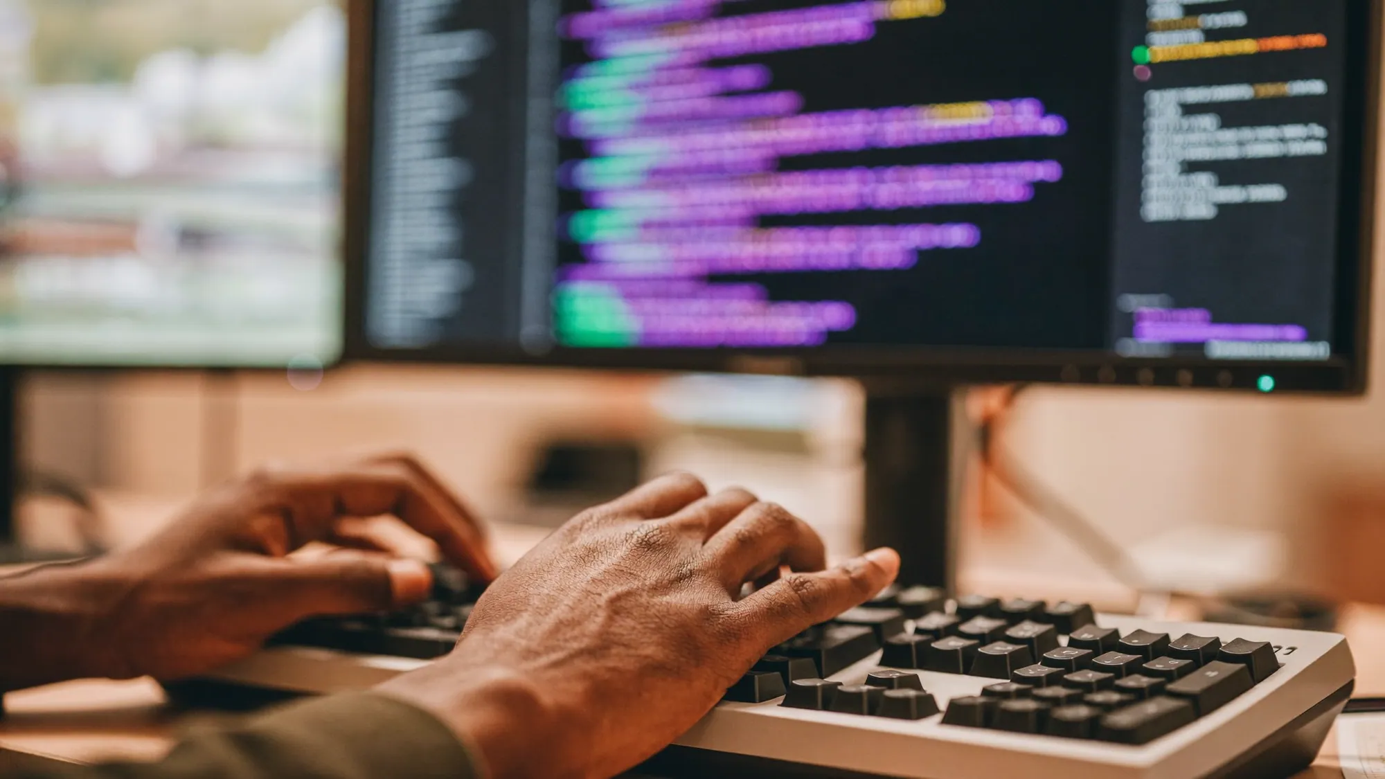 A web developer's hands on a keyboard with code on screen, illustrating what web development is