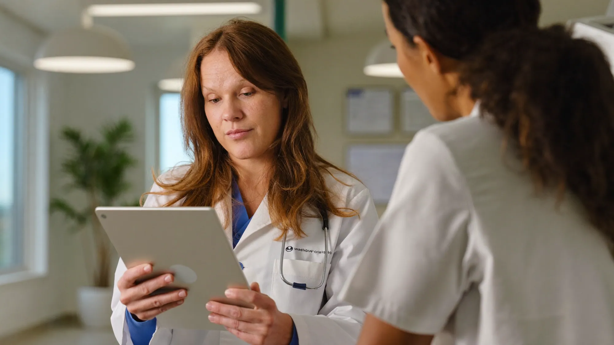 A doctor using a tablet running custom HIPAA-aware healthcare software in a clinic during a clinical workflow