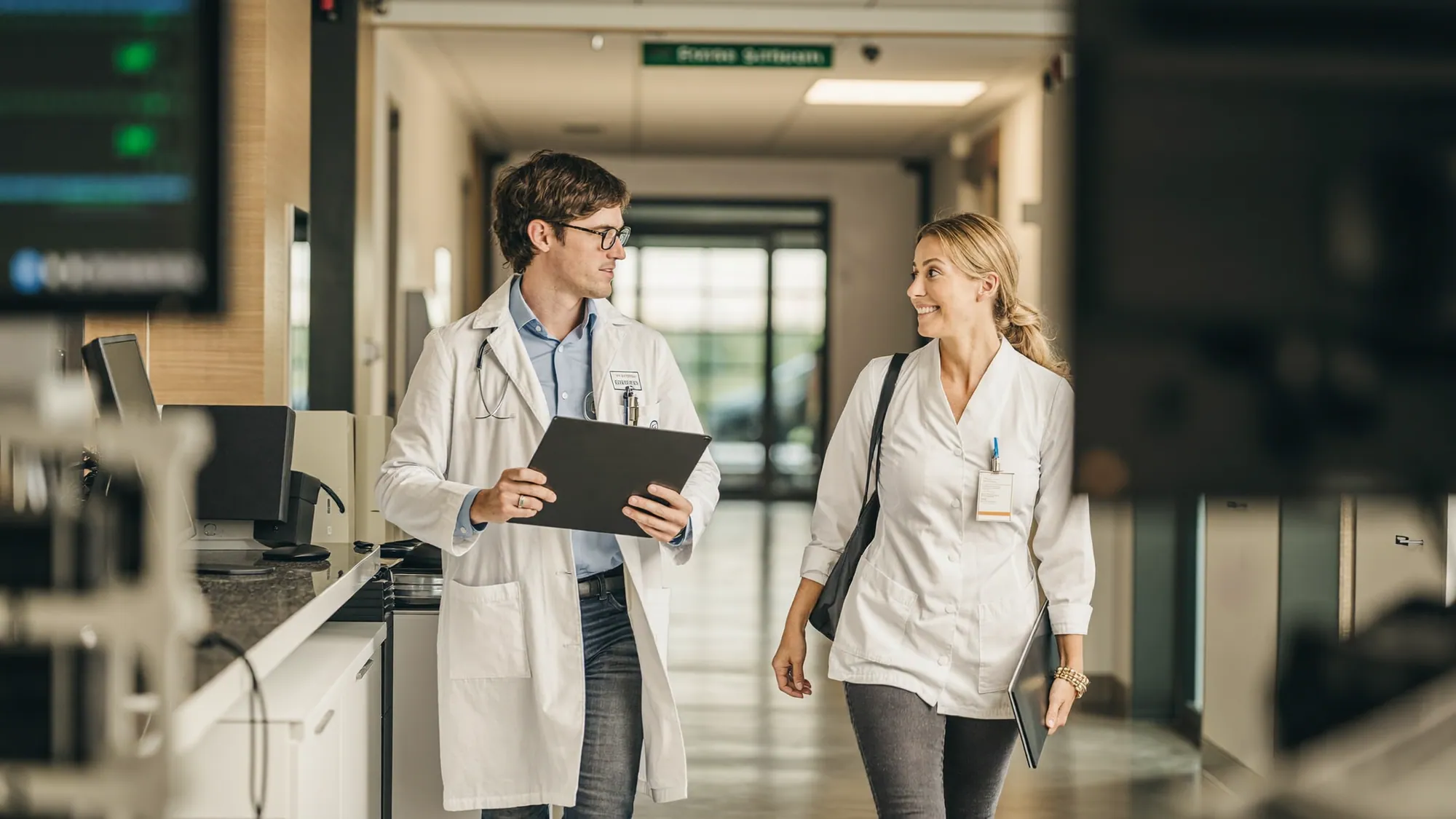 Un médico y un profesional de TI hospitalaria colaborando en un pasillo de hospital sobre transformación digital en la atención clínica