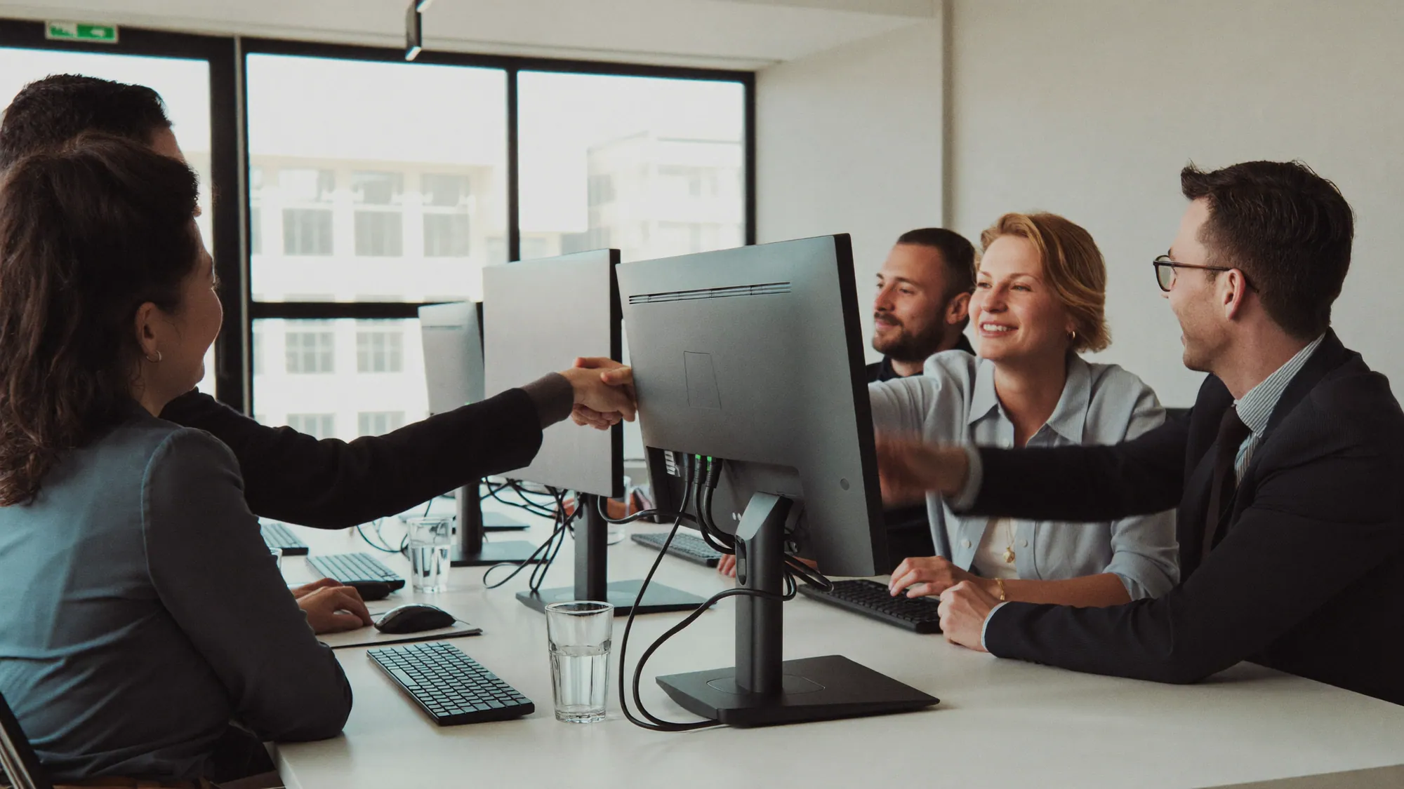 A business client and a custom software development team shaking hands across a table after evaluating the partnership