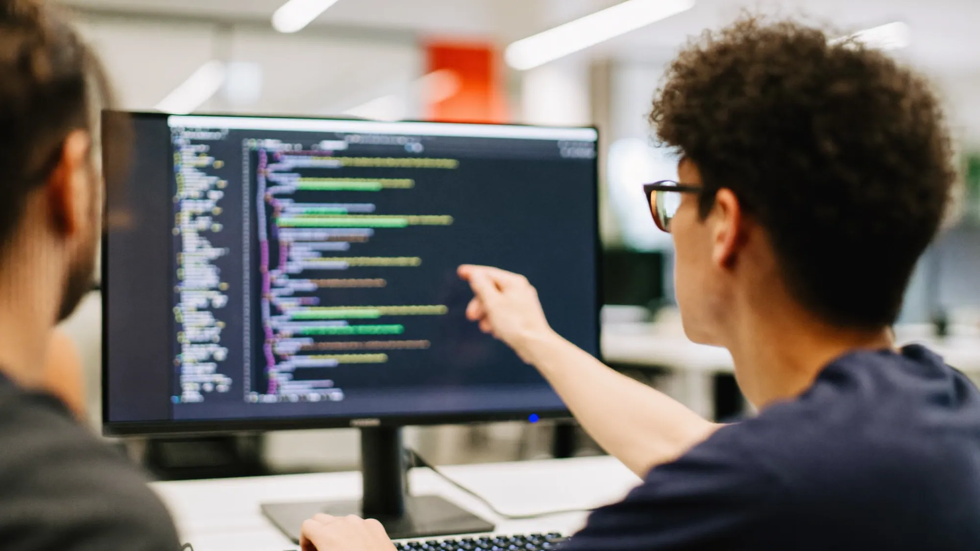 Two nearshore developers pair-programming, one pointing at code on a monitor, showing the senior talent behind the hourly rate